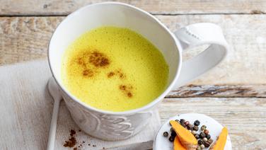 Ein Becher Goldene Milch steht zusammen mit Gewürzen auf einem Tisch.  Foto: Claudia Timmann/ZS Verlag