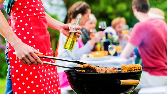 Person holds apron at grill, people eat and drink in background.  © Fotolia Photo: Kzenon
