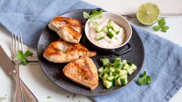 A plate with three pieces of chicken breast and a bowl with dressing and diced cucumber are on the table.  © NDR Photo: Claudia Timmann