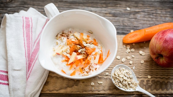 Eine Schüssel mit Joghurt-Hafer-Frühstück steht auf dem Tisch, danaben eine Möhre und ein Apfel. © NDR Foto: Claudia Timmann