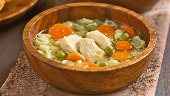 A wooden bowl of chicken soup with a tea towel underneath.  © imago images Photo: Panthermedia