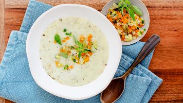 A plate of creamy potato soup with diced vegetables and marjoram on a wooden table.  © NDR photo: Claudia Timman