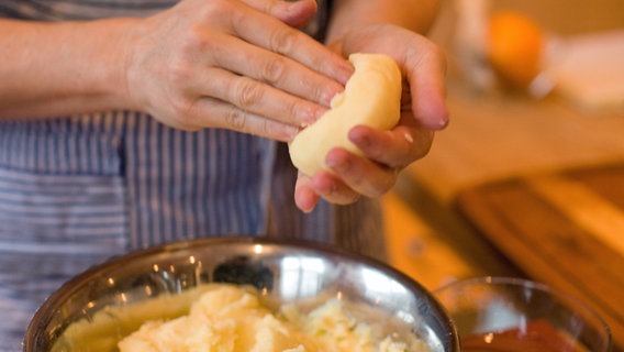 Ein Koch drückt eine Mulde in einen Kartoffelkloß. © NDR Foto: Claudia Timmann