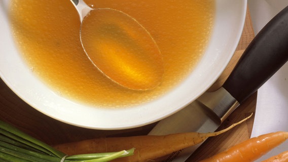 A plate of clear broth next to carrots and chives.  © picture-alliance/dpa/Stockfood Photo: FoodPhotography Eising
