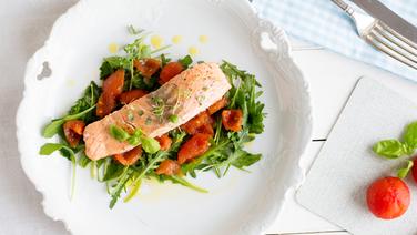 Ein Teller mit  Lachsfilet auf geschmolzenen Tomaten und Rukolablätter steht auf dem Tisch. © NDR Foto: Claudia Timmann