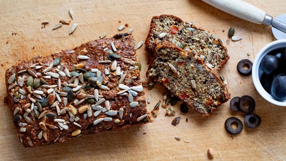 Eiweißbrot und schwarze Oliven auf einem Holzbrett. © NDR Foto: Claudia Timmann