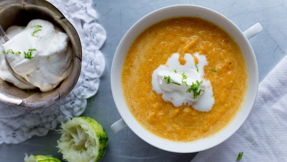 Eine Suppenschüssel mit Möhren-Ingwersüppchen und ein Schälchen mit Limettensahne stehen auf dem Tisch. © NDR Foto: Claudia Timmann