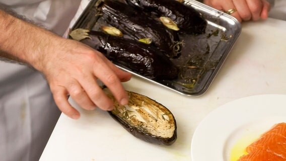 Ali Güngörmüs zeigt im Ofen gegarte Auberginenhälften. © NDR Foto: Claudia Timmann