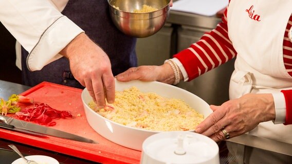 Ein Koch verteilt Streusel auf Rhabarberstücke in einer Auflaufform. © NDR Foto: Claudia Timmann