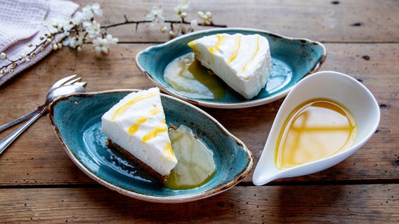 Two pieces of New York cheesecake in small bowls, next to a gravy boat with passion fruit sauce.  © NDR Photo: Claudia Timmann