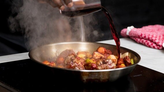 Gemüse für einen Soßenansatz wird mit Rotwein in der Pfanne abgelöscht. © NDR Foto: Claudia Timmann