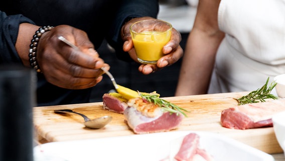 Ein Koch streicht Senf auf ein Stück Lammfleisch. © NDR Foto: Claudia Timmann