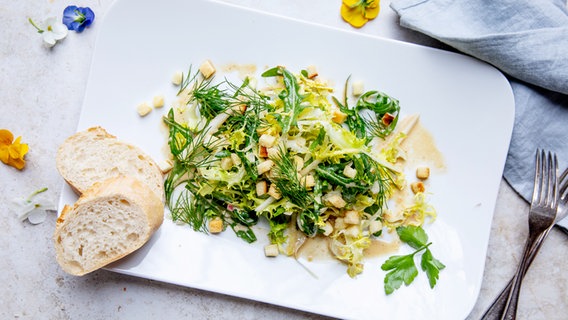 Ein Porzellan-Teller mit frischem Salat und zwei Scheiben Baguette auf einem Holztisch. © NDR Foto: Claudia Timmann