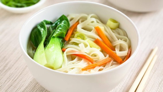 An Asian dish of pak choi, noodles and carrot sticks in a white porcelain bowl.  © Panthermedia / imago Photo: xildix