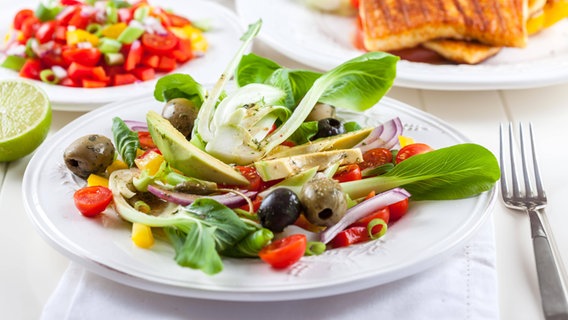 A porcelain plate with a salad of pak choi, olives, avocado and tomatoes on a laid table.  © Panthermedia / imago Photo: Brebcax