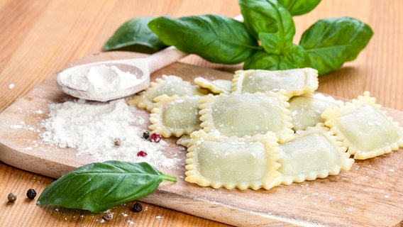 Homemade ravioli lie on a wooden board with basil.  © Colourbox photo: Motorolka