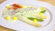 Ein Stück pochierter Schellfisch ist mit Spargel, Bärlauch-Schaum, Kartoffel-Kugeln und Tomaten-Confit auf einem weißen Teller angerichtet. © NDR 