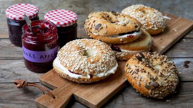 Mit Frischkäse und Marmelade bestrichene Bagels auf einem Holzbrett. © NDR Foto: Claudia Timmann