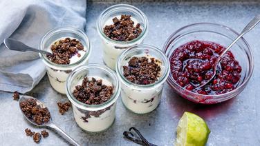 Vier Gläser mit Schmand-Mousse und Pumpernickel-Crumble, daneben eine Schale mit Beerengrütze. © NDR Foto: Claudia Timmann