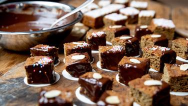 Verzierte braune Kuchen liegen auf einem Holztisch. © NDR Foto: Claudia Timmann