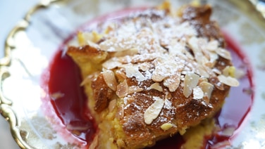 Bread pudding served on a plate with powdered sugar, almond pieces and raspberry sauce.  © NDR 
