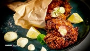 Fried chicken with lemon and mayo served on a plate.  © NDR 