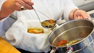 Léa Linster seiht Suppe durch ein Mulltuch kocht in einem Topf © NDR Foto: Claudia Timmann