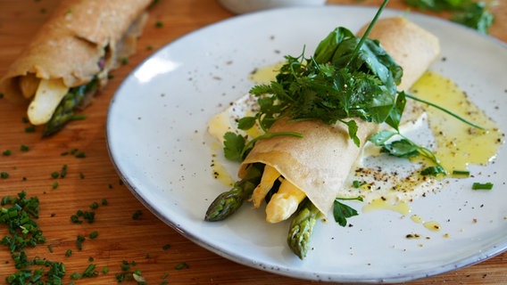 A buckwheat pancake filled with green and white asparagus lies on a tray.  © NDR Photo: Florian Crook