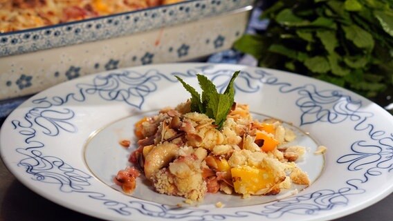 Crumble mit Banane, Mango und Erdbeeren auf einem weiß-blauen Teller © NDR Foto: Florian Kruck