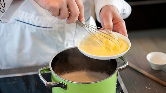 In einem Topf kocht Milch, daneben ein Teller mit einer gelben Masse. © NDR Foto: Claudia Timmann