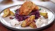 Frittierter Fisch liegt auf Rotkohlsalat. Daneben liegen gebackene Kartoffelspalten. © NDR Foto: Franziska Husmann