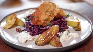 Frittierter Fisch liegt auf Rotkohlsalat. Daneben liegen gebackene Kartoffelspalten. © NDR Foto: Franziska Husmann