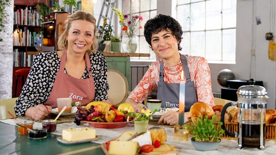 Zora Klipp und Theresa Knipschild sitzen an einem reich gedeckten Frühstückstisch. © NDR Foto: Claudia Timmann