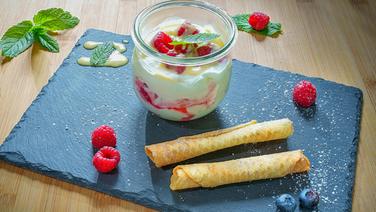 Raspberry meringue in a glass with waffle rolls and berries on a dark slate © NDR/doclights Photo: Marc Vorwerk