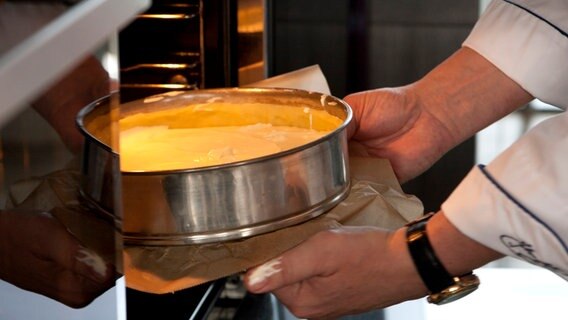 Ein Bäcker schiebt einen Käsekuchen in einen Ofen. © NDR Foto: Claudia Timmann
