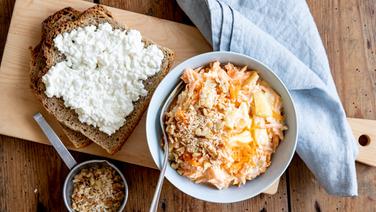 Karottensalat und eine Scheibe Brot mit Hüttenkäse auf einem Holzbrett. © NDR Foto: Claudia Timmann