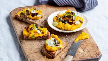 Drei Scheiben Brot mit  Kürbisaufstrich, garniert mit Kürbiskernen, auf einem Holzbrett.  Foto: Claudia Timmann / ZS Verlag