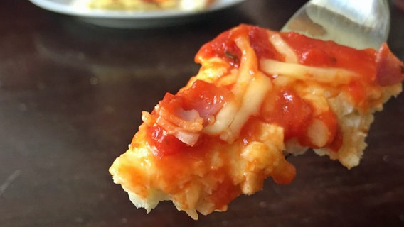Ein Stück Pizza mit Tomatensoße und Käse belegt auf einer Gabel. © NDR Foto: Nicole Hoenig