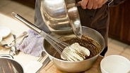 Ein Koch füllt Eischnee in eine Schüssel mit Schokoladencreme. © NDR Foto: Claudia Timmann