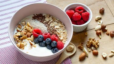 Eine Schale mit einem Müsli mit Skyr und Heidelbeeren und Himbeeren sowie Nüssen. Daneben ein Schälchen mit Himbeeren. © NDR Foto: Claudia Timmann