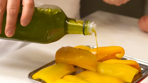 Über geviertelte Paprikastücke wird Olivenöl gegossen. © NDR Foto: Claudia Timmann