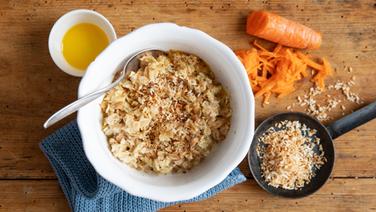 Eine Schale mit Hafer-Porridge mit gerösteten Kokosflocken, daneben eine geraspelte Möhre. © NDR Foto: Claudia Timmann