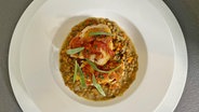 Geschmorte Poularde mit Tomatensoße und Linsen auf einem weißen Teller © NDR 