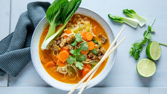 Eine Schale mit Curry-Ramen-Suppe, am Schalenrand ein Blatt Pak Choi sowie ein paar Stäbchen. © NDR Foto: Claudia Timmann