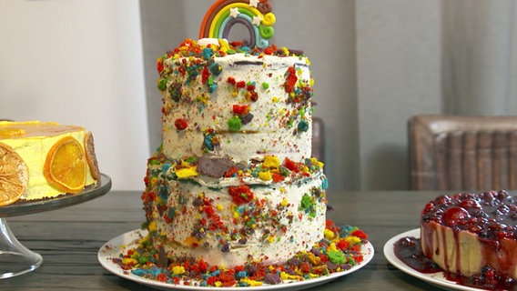 Ein hoher Regenbogen-Kuchen steht auf einem Tisch. © NDR 