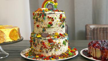 A tall rainbow cake stands on a table.  © NDR 