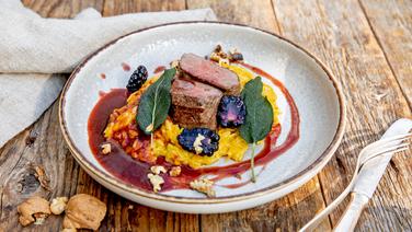 Saddle of venison with pumpkin risoni and blackberries served on a plate.  © NDR Photo: Claudia Timmann