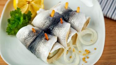 Three rollmops lie on a white plate, next to them are onions, mustard seeds, lemon and parsley.  © colourbox 