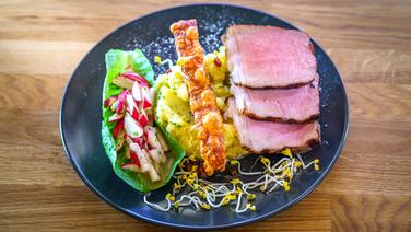 Gegrilltes Schweinekotelett mit knuspriger Schwarte, Kartoffelstampf und Salat auf einem Teller serviert. © NDR/Doclights GmbH Foto: Marc Vorwerk