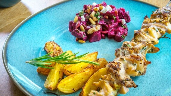 Gegrillte Störspieße mit Kartoffelspalten und Rote-Bete-Salat auf einem Teller angerichtet. © NDR Foto: Marc Vorwerk